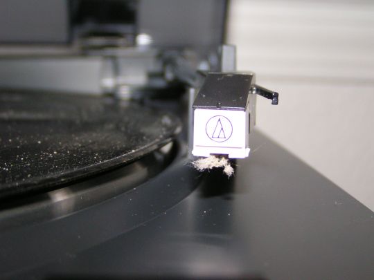 Close-up photo shows the Audio-Technica AT-3600L cartridge. The stylus is covered in dust. Dust is also visible on the LP sitting on the adjacent turntale platter.