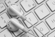 Marco photograph of earbud-style headphones resting on the '5' and 'R' keys of a similarly colored laptop keyboard.