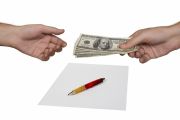 Photo shows pen atop a contract. Above, one hand offers a stack of one hundred dollar bills to another hand.