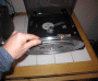 Photo shows a hand holding up a platter with a rubber drive belt wrapped around the bottom. The unassembled Audio-Technica AT-LP2D-USB turntable is in the background.