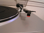 Close-up photo of the cartridge and stylus on the Ion Audio TTUSB05 turntable. Platter with mat is partially visible on left side of photo.
